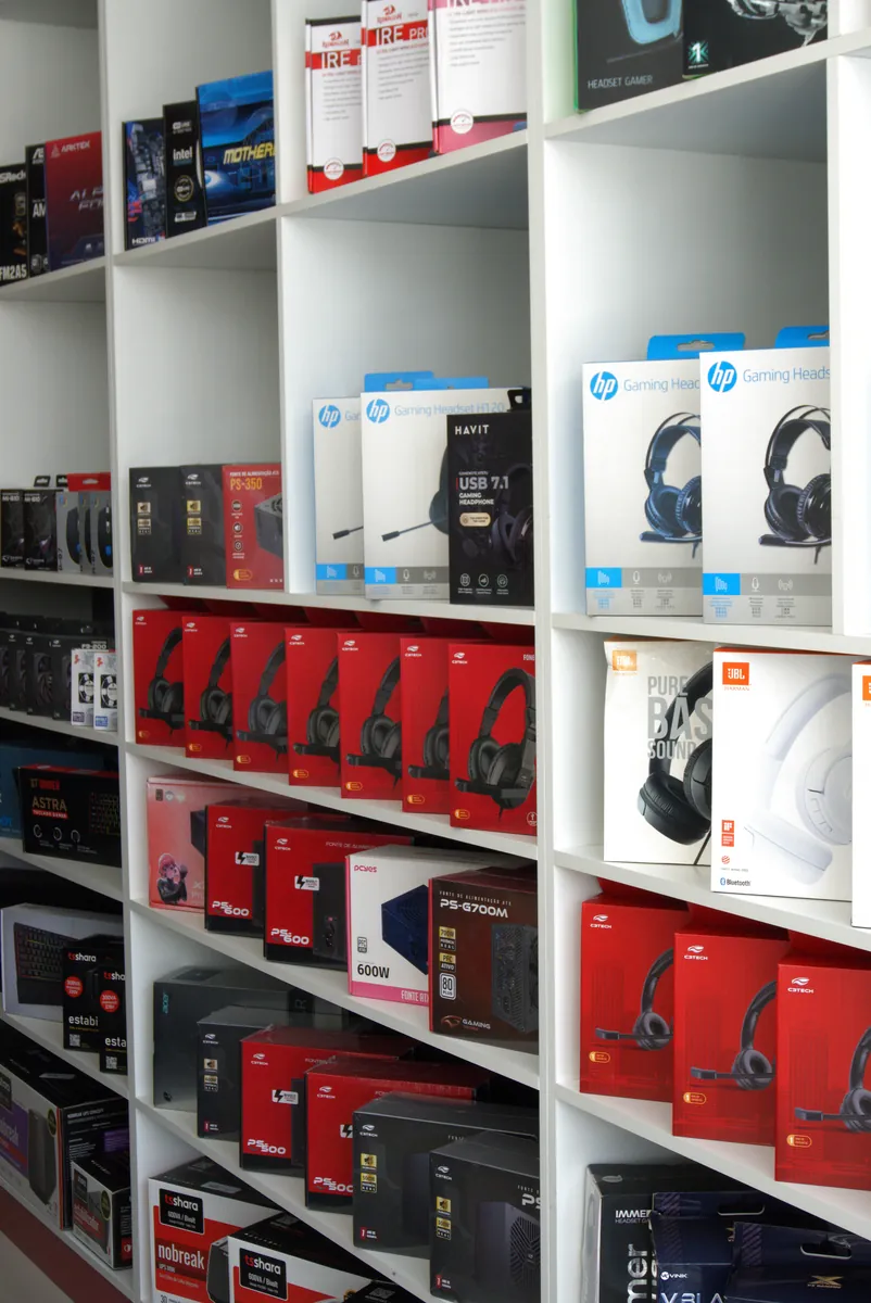 Prateleiras com headsets gamer HP, JBL e C3Tech, fontes de alimentação e placas-mãe